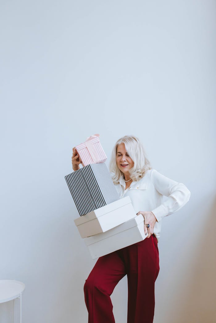 Elegant elderly woman smiles while carrying gift boxes in a stylish indoor setting.